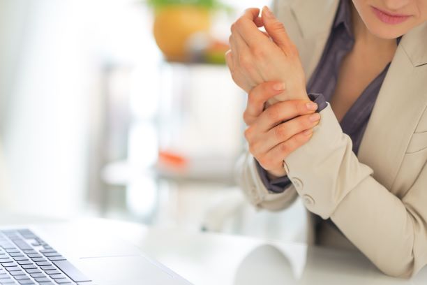 woman holding injured wrist while sitting in front of computer keyboard